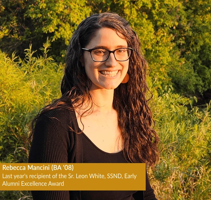 Rebecca Mancini, BA '08, is the last year's recipient of the Sr. Leon White, SSND, Early Alumni Excellence Award. She is smiling as she is wearing a black top with green foliage in the background illuminated by warm sunlight.