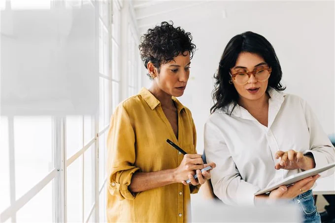 Two professionals reviewing a document on a digital tablet in a bright office space.