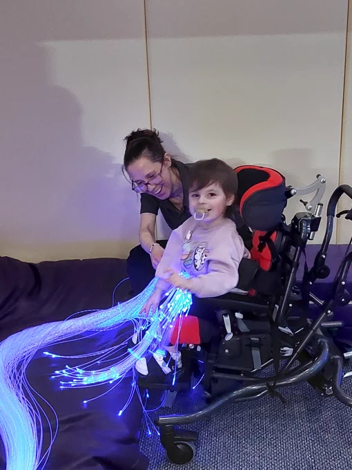 Girl in wheelchair using fibre optic strands in sensory room at High Rise Lisburn