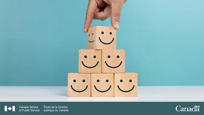 Image depicting a hand stacking blocks with smiley faces on them. 