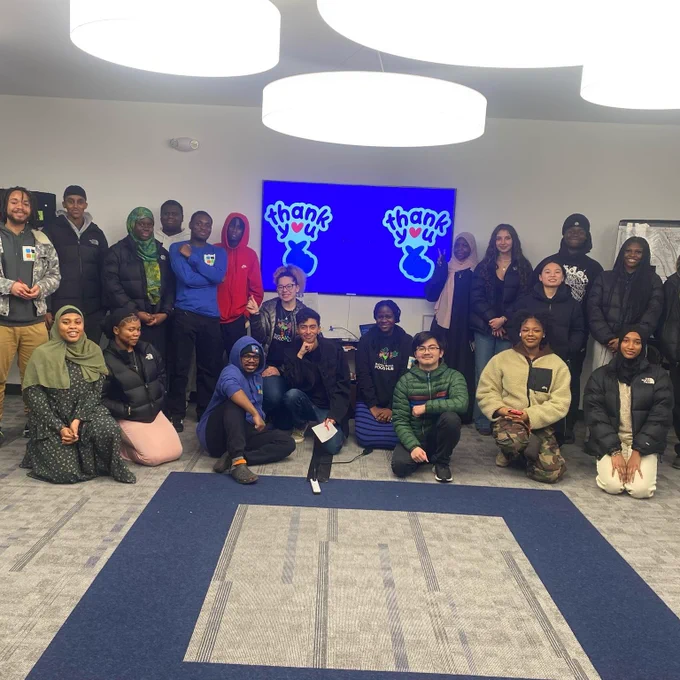A diverse group poses in front of a display with "thank you" text indoors.
