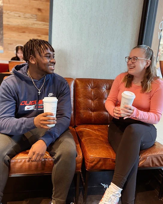 Students smiling next to each other on a couch and holding coffee cups