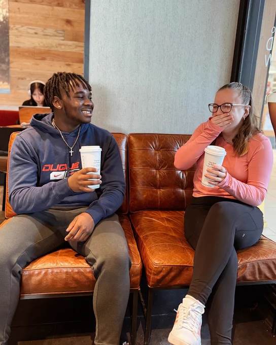 Students smiling next to each other on a couch and holding coffee cups