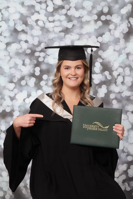 A woman wearing grad regalia and a UFV certificate poses for the camera.