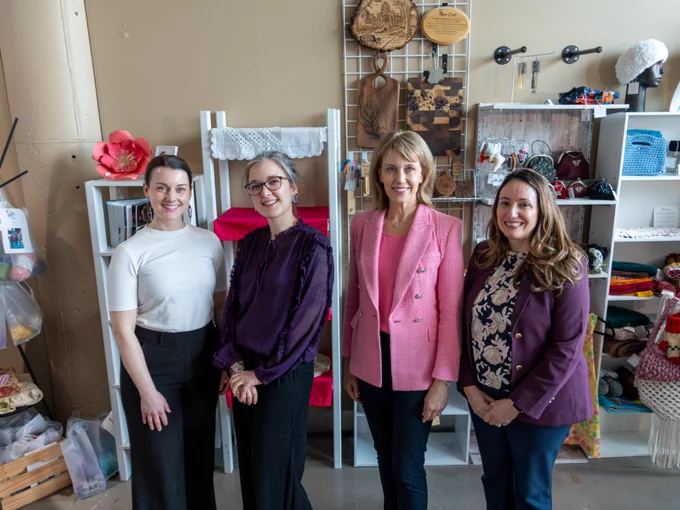 Four individuals smiling and standing in a craft store surrounded by various handmade goods on shelves.
