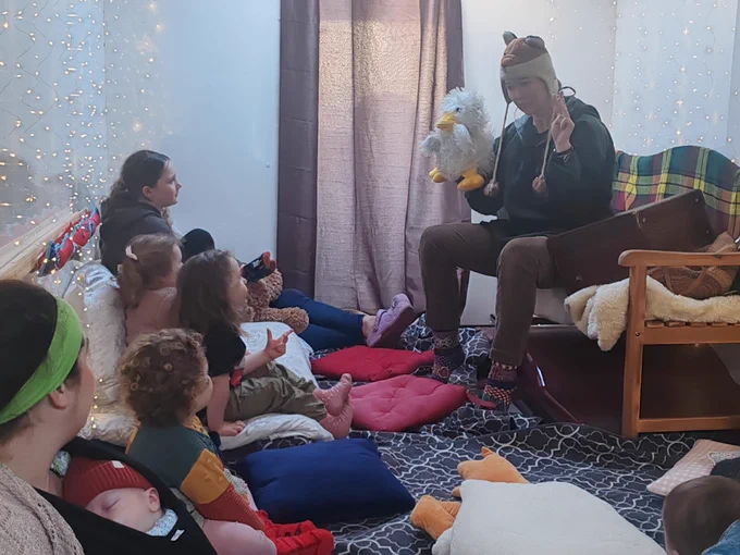 Community members listen on to a storytelling session on the Spark Bus. The storyteller is holding a toy duck. 