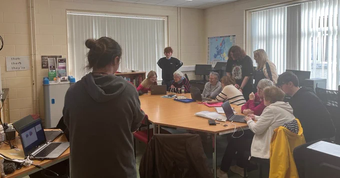 Young and older people working on computers around a table