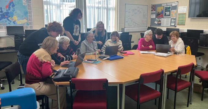 Young and older people working on computers around a table