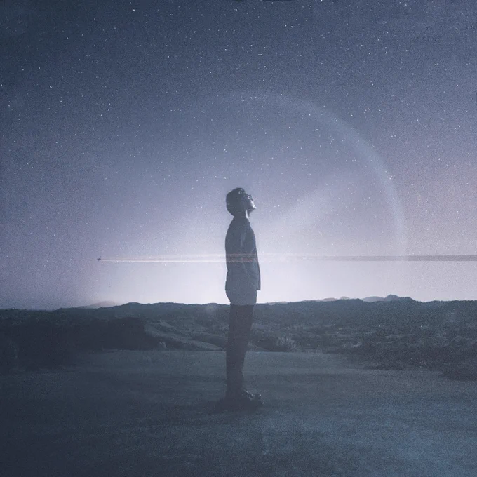 Levi Patel - Sailing on the Light of a Passing Star album cover. Levi stands sideways, looking upwards, in front of a starry night sky with hills in the background. Mostly blue/grey tones, and with a faint circular light around him, and a plane flying through the centre of the image.