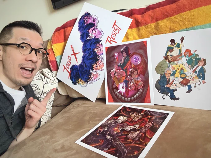 Selfie with some prints of my art laid out on the couch. There are prints of fanart from 1000xRESIST, Mouthwashing, Severance, and Elden Ring. 
