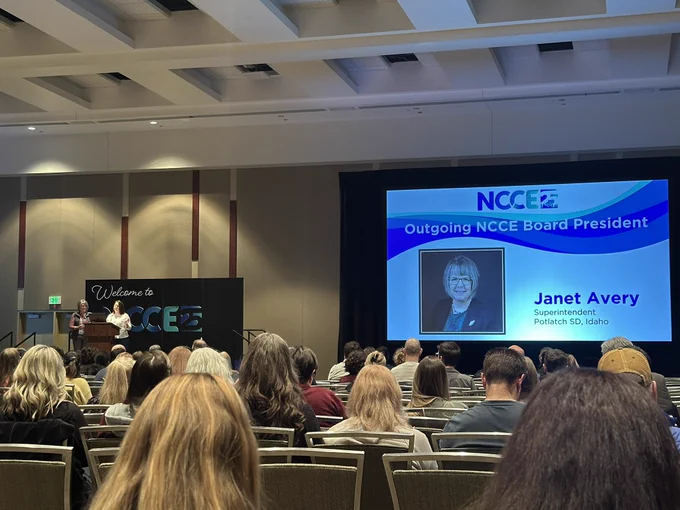 A picture of a stage and a screen showing a picture of Janet Avery being recognized for her work as outgoing board president of NCCE.