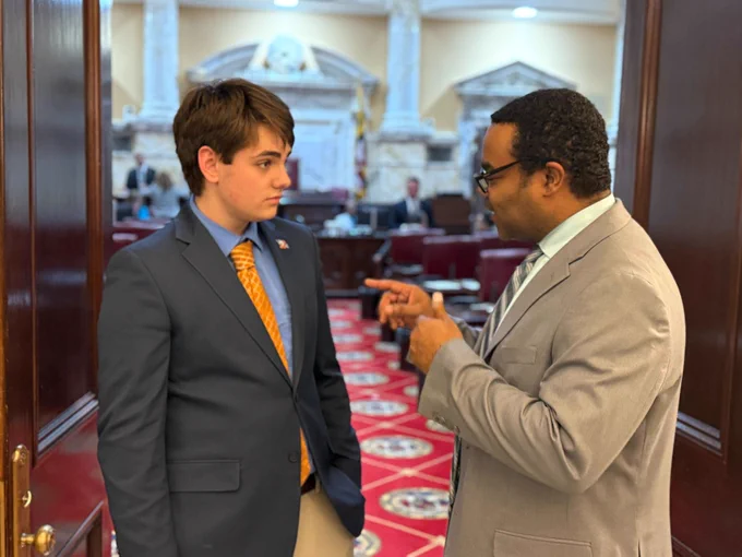 A Black male State Senator deep in conversation with a teen boy.
