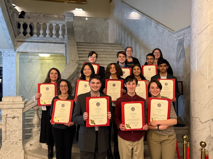 A group of about ten high school and middle school students hold up their certificate of citation at the Maryland State House.
