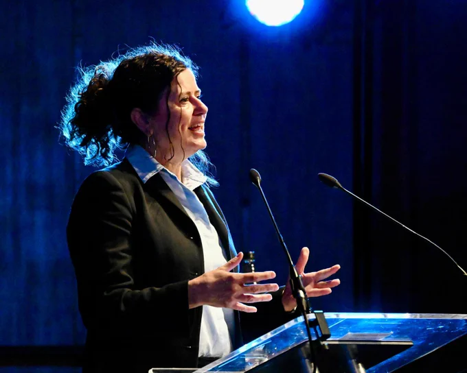 Cllr Claire Holland, Chair of London Councils and Leader of Lambeth Council, speaking at the launch of the London Growth Plan at Imperial College London. She is wearing a black suit and a white shirt, speaking from a lectern with two microphones.
