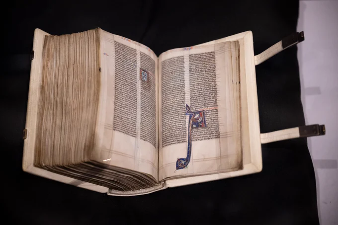 The Sarum Master Bible on display at the reception, resting on a black book cushion (folio 585r. Apocalypse, with initial of St John as a medieval scribe, writing his Revelation.  Image Finnbarr Webster, courtesy of Salisbury Cathedral.