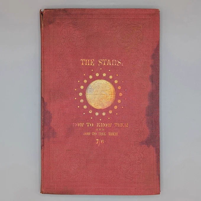 Photograph depicting the red cover of a book, with the title in gold lettering and a gold illustration of a globe surrounded by stars.