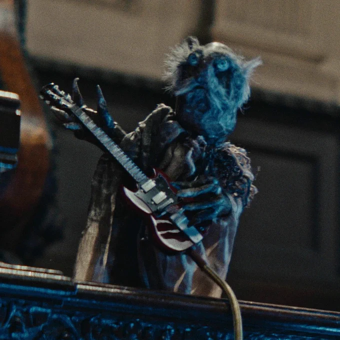 A strange puppet with staring eyes a white handlebar moustache and a dirty monks habit, playing a gibson SG guitar in a church, illuminated by spectral blue light.