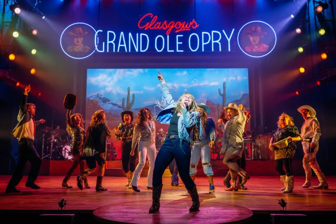 An onstage country and western scene with dancing cowboys and cowgirls, a singer centre stage and a backdrop with cactus behind