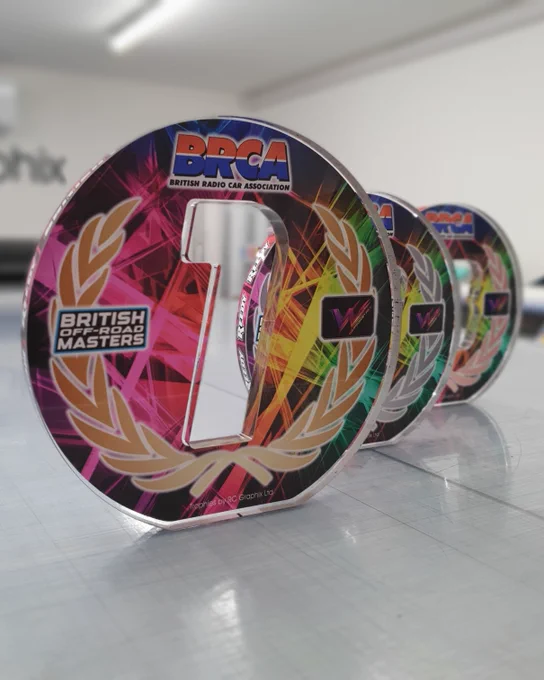 Freestanding acrylic trophies featuring colourful graphics and BRCA branding.  The trophy in the foreground has a number '1' cut of of the centre.