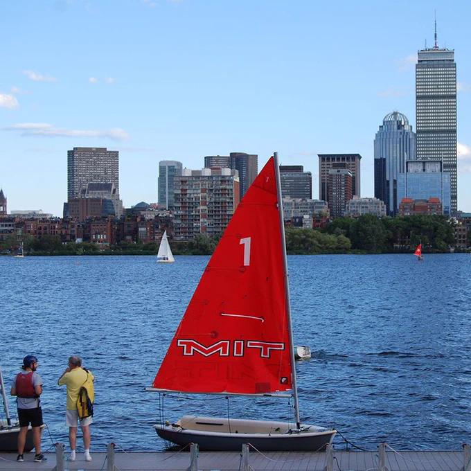 MIT sailboat on the Charles River with the Boston skyline in the background.