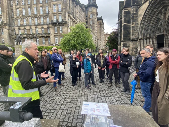 A group of people standing outside a historic stone cathedral, grouped around a guide who is giving them information.