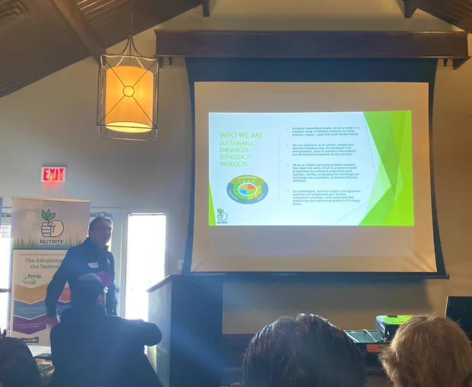 Ken stands next to a PowerPoint slide