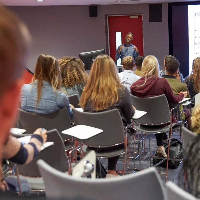 A photograph of a group of people in a lecture theatre looking at a tutor and presentation.