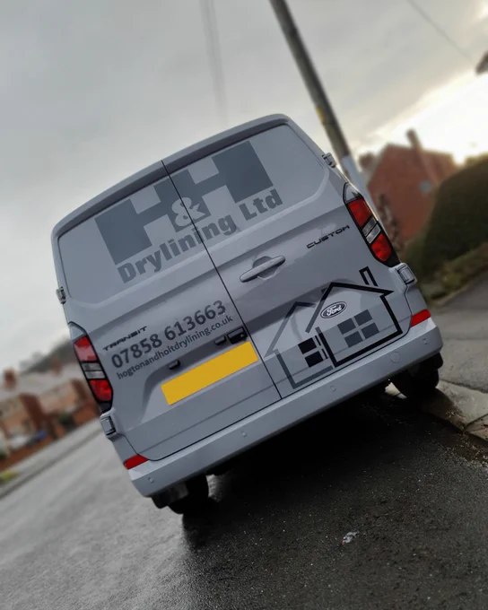 Rear of a grey Ford Transit van, featuring 'H&H Drylining Ltd' dark grey graphics doors and an outline of 2 houses on the doors.