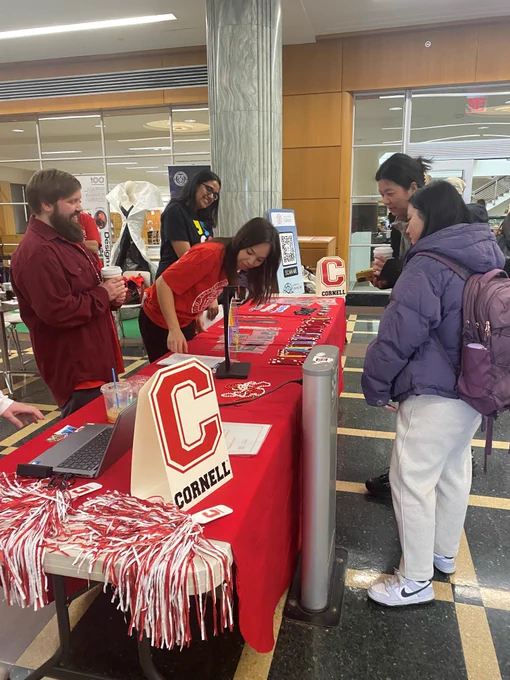 Students and staff playing a trivia game in the Mann Library lobby. Table is covered with various prizes and a Cornell "C" sign. 