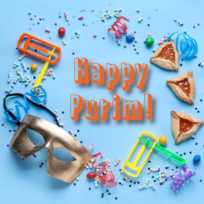 A flat lay image featuring a gold masquerade mask, colorful noise makers, and various festive candies on a light blue background. Three triangular hamantaschen pastries are arranged alongside the text "Happy Purim!" in bold orange letters.