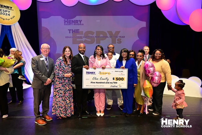 Winner receives check with sponsor, family, and district leadership.