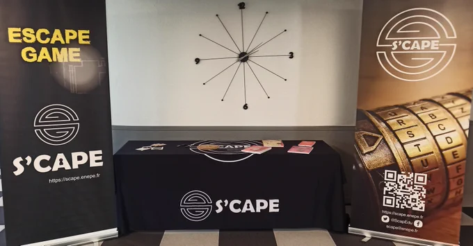 La photo montre un stand de présentation dédié aux escape games éducatifs, sous la bannière de S'CAPE. Deux roll-ups encadrent une table recouverte d'une nappe noire arborant le logo de l'organisation.

🔹 À gauche, un kakémono noir porte l’inscription "ESCAPE GAME" en lettres jaunes, avec le logo S'CAPE et l’URL de leur site web.

🔹 À droite, un second kakémono affiche une image d’un cryptex (un dispositif de verrouillage à lettres utilisé dans les escape games) et les coordonnées de S'CAPE, y compris un QR code pour accéder à leur site.

🔹 Au centre, la table contient divers objets liés aux escape games :

Un disque en bois qui semble être une roue de chiffrement.
Plusieurs livrets et documents posés sur la nappe.
Une paire de lunettes et d’autres accessoires.
🔹 En arrière-plan, une horloge murale design, faite de tiges métalliques avec les chiffres 3, 6, 9 et 12, ajoute une touche esthétique et évoque peut-être la gestion du temps dans un escape game.