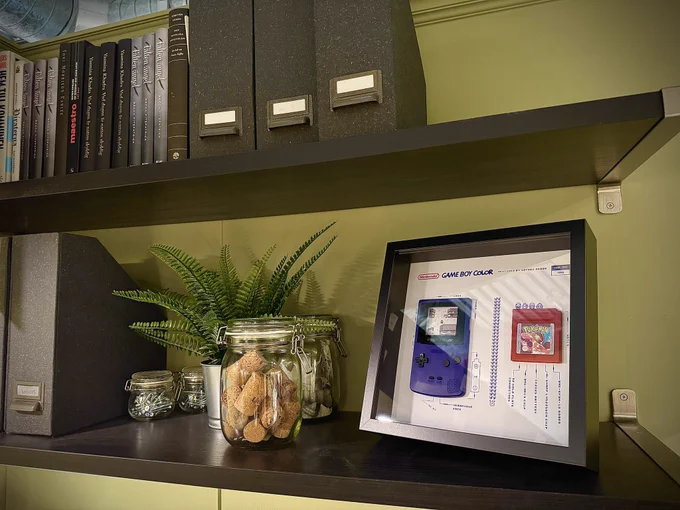 A purple Game Boy Color on display with a red Pokemon cartridge, on an office book shelf