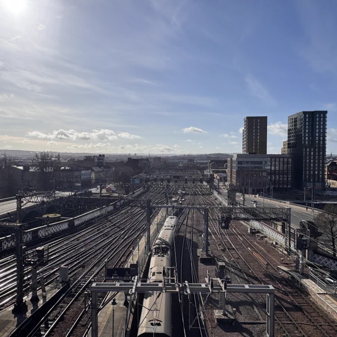 View of railway tracks leading into Glasgow Central station with surrounding cityscape and high-rise buildings under a clear blue sky.