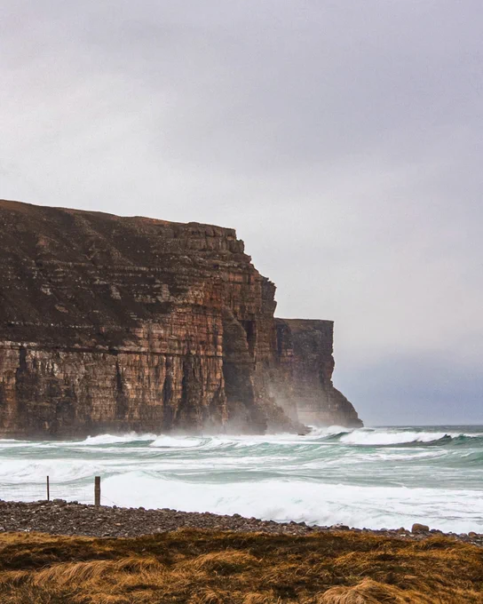 View over the bay at Rackwick, with wild seas rolling in and large sandstone cliffs behind. 