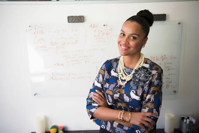 a photograph of a young woman standing in an office with flip chart paper on the walls, she is smiling at the camera 