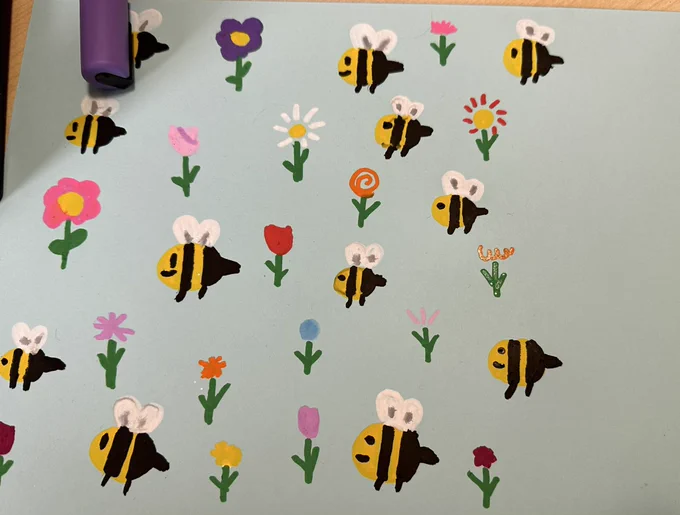 A close up of light blue paper  with recurring hand-drawn bright images of bumble bees and flowers.