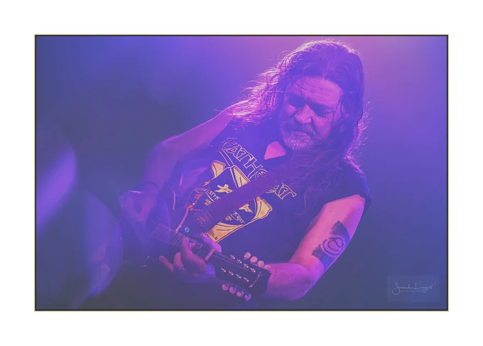 Pete Bailey playing the mandolin at a Leatherat gig at The Star Inn in Guildford, Surrey. The stage lights have bathed Pete in purple tones. I added some refracted light into the composition using a creative photography system by Lensbaby, which has a variety of light changing materials, including crystals, called the Omni system. The result in this piece is several semi-circular bokeh (blurred) light areas that cut through the deepest purples in the lower left corner. Pete has long wavy hair and a short beard. His hair is caught with gold highlights from a spotlight at the front of the stage and I used a selection masking tool to bring back the yellow colour of the t-shirt design with the Leatherat logo. Leatherat play energetic music that's a fusion of folk, rock and punk! 