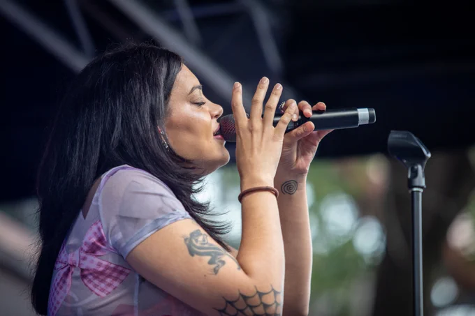 Thelma Plum sings into a microphone from the right side profile, her eyes are closed with feeling.