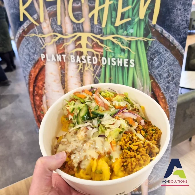 Hand holding a bowl of macaroni and cheese and salad by a banner that says plant-based dishes.