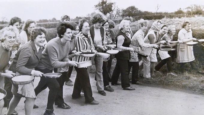 Black and white photograph of a group of people lined up for a pancake race