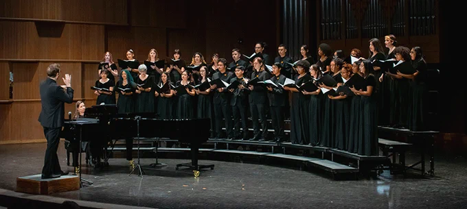 Choir performing on stage with conductor directing in front.