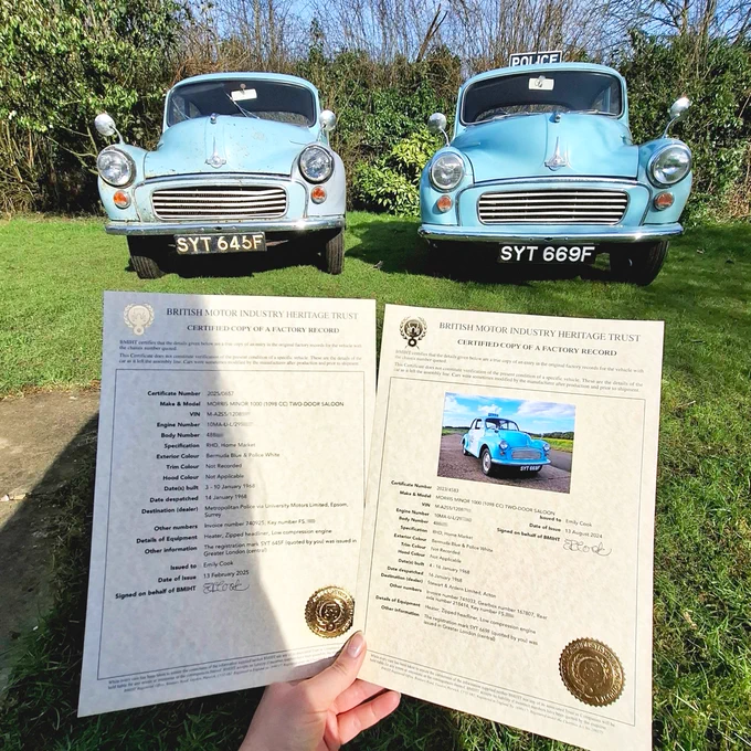 Two BMIHT Heritage Certificates, one standard, one with a photo, being held up in front of two Morris Minor police cars