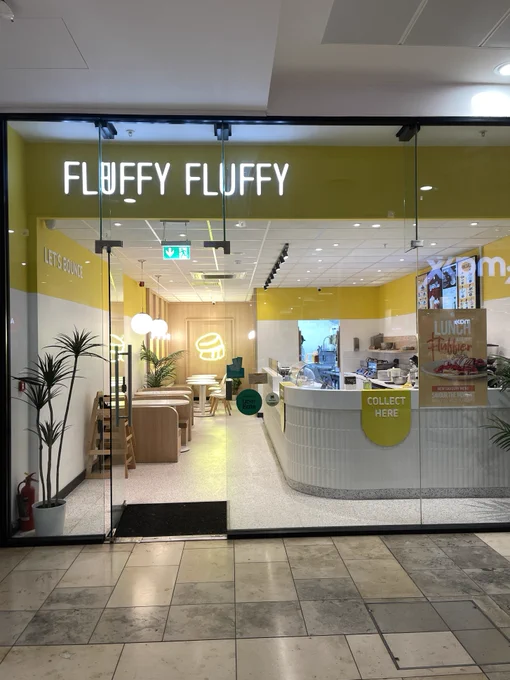 Entrance to Fluffy Fluffy café with transparent glass doors and a modern interior, featuring bright lighting and minimalist furniture.