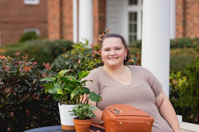 Person sitting at a table with potted plants, near a building with white columns.