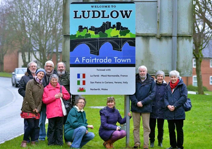 Volunteers from the Fairtrade Ludlow gathered  stand with the town's colourful fairtrade road sign. 