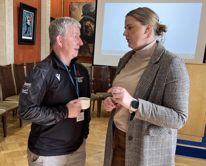 Image of two people – Junior Minister Aisling Reilly chatting to Des Jennings of Commonwealth Games NI at the event in Parliament Buildings celebrating the positive impact National Lottery funding has had on many local arts, community, heritage and sporting projects over the past three decades.