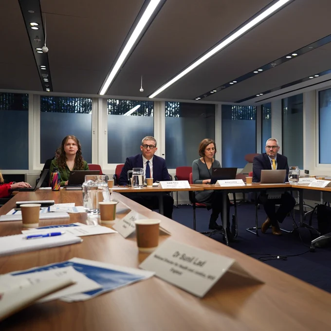 Lord Timpson sat with senior advisors with notepads, and laptops in front of each, in a well-lit room with overhead lights and glass walls.