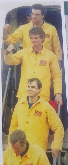 POWs in yellow suits walk from a Red Cross aircraft 