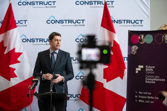 Future Skills Centre's Noel Baldwin speaking at a podium with two Canadian flags in the background. 